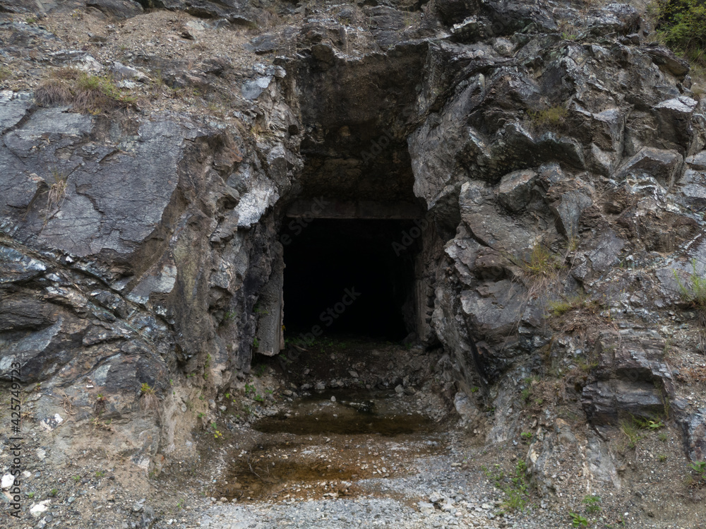 Abandoned industrial mines entrance, dark spooky asbestos shaft in rock, dangerous urban exploration, asbestos cancers