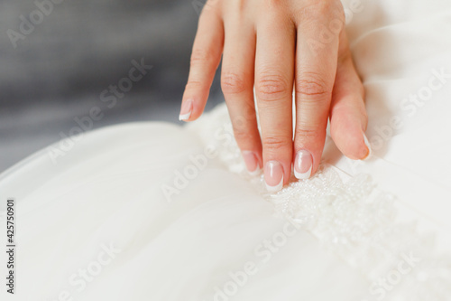 Bride's hand touching details of her wedding dress. Simple french manicure