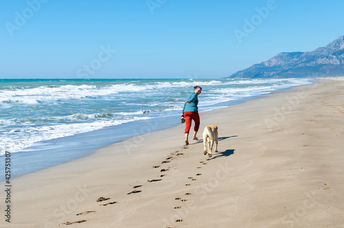Footprints on the sand foot of a girl walking with sneakers in hand. Girl running with a dog on the Patara beach, Turkey