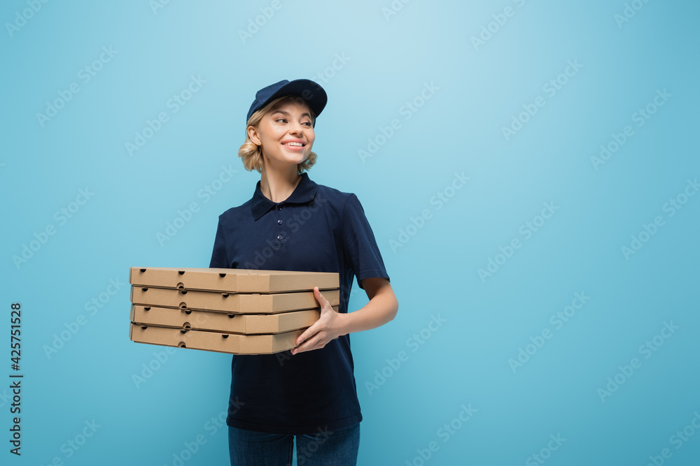 pretty courier holding pizza boxes while looking away isolated on blue pretty courier holding pizza boxes while looking away isolated on blue