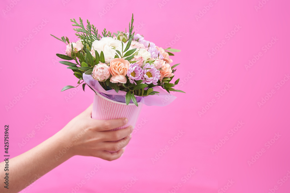 Beautiful bouquet of mixed different flowers in hand on pink background, greeting, gift