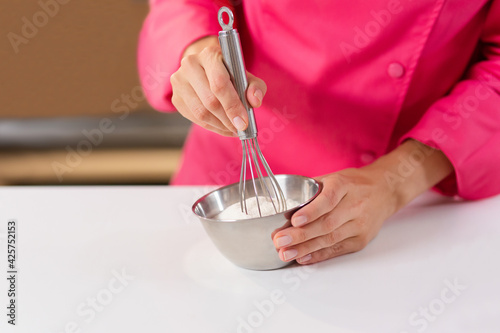 Girl baker, pastry chef, cook prepares dough for baking. Woman stirring dough in stainless bowl with a whisk.
