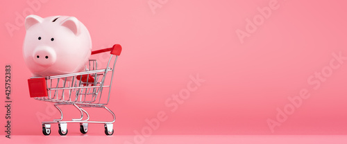 Fotografía Pink piggy Bank with a shopping cart stands on a pink background, Online business shopping concept