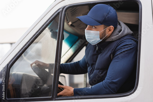 arabian delivery man in medical mask looking ahead while driving truck