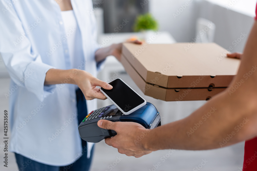 cropped view of delivery man holding payment terminal and pizza boxes near woman with mobile phone cropped view of delivery man holding payment terminal and pizza boxes near woman with mobile phone