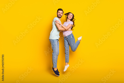 Full length body size view of attractive trendy cheerful couple jumping hugging isolated over bright yellow color background