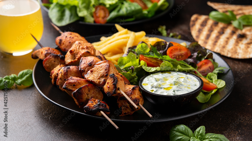 Chicken fillet souvlaki, kebabs on skewers with potato chips, salad and fresh home made tzatziki Chicken fillet souvlaki, kebabs on skewers with potato chips, salad and fresh home made tzatziki