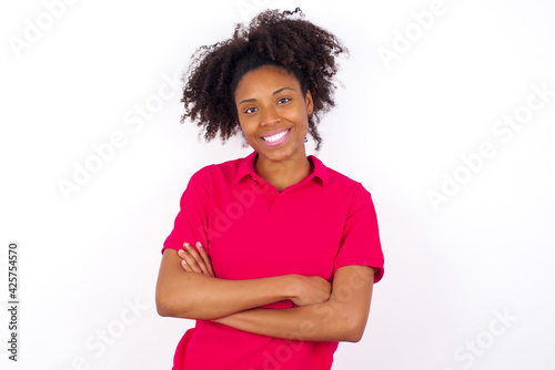 young beautiful African American woman wearing pink t-shirt against white wall being happy smiling and crossed arms looking confident at the camera. Positive and confident person.