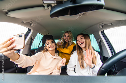 Three women having fun in the car and taking selfies with phone