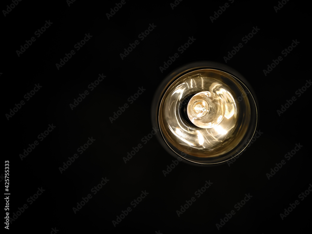 Selective focus yellow light bulb in round chandelier on black background. Warm and cozy atmosphere in dark interior. Abstract background. Selective focus yellow light bulb in round chandelier on black background. Warm and cozy atmosphere in dark interior. Abstract background.