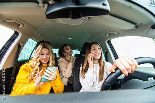 Three best friends women in the car and uses smart phones while drive car in road trip