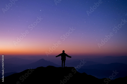 Silhouette of happy woman open hands against and watched night sky, star and milky way background alone on top of the mountain. People having fun on summer vacation freedom and imagination concept.