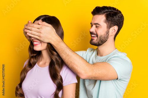 Portrait of attractive cheerful couple guy closing girl's eyes prepare surprise isolated over bright yellow color background