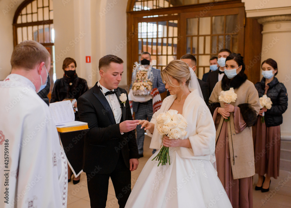 Fototapeta premium Front view of church wedding ceremony of newlyweds. The groom puts a ring on the bride's finger. Concept of wedding traditions