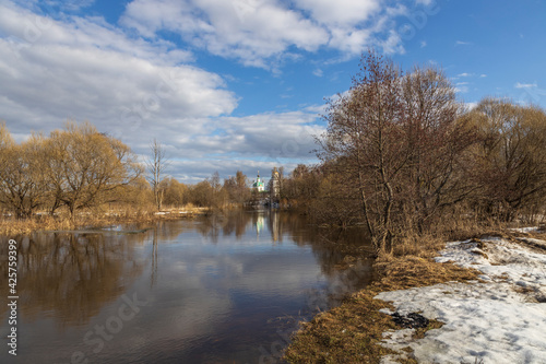 Spring flood. High water. Church on the banks of the river. Rural landscape in early spring. Clouds and trees reflected in the water.