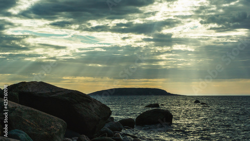 The sun's rays break through the clouds above the sea surface. Seascape with dramatic sky. Shoreline with large boulders in the evening light. Russia, the White Sea.