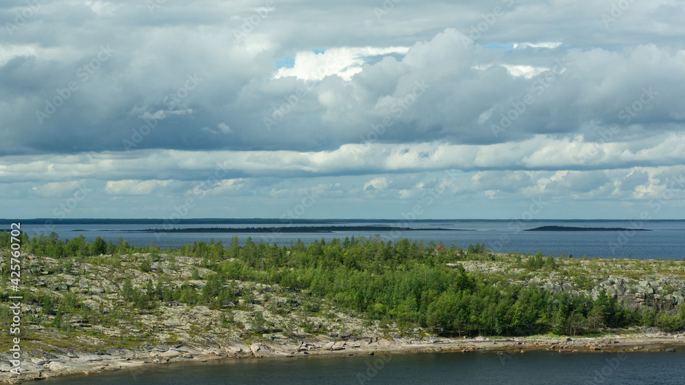 View of the sea and sky from a high point. Harsh northern nature. Rocky island overgrown with forest, dramatic sky with rain clouds. Beautiful view of the White Sea, Russia. View of the sea and sky from a high point. Harsh northern nature. Rocky island overgrown with forest, dramatic sky with rain clouds. Beautiful view of the White Sea, Russia.
