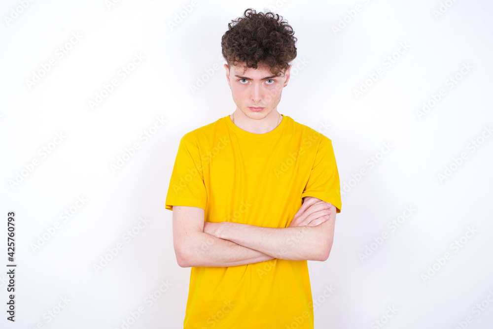 Serious pensive young caucasian handsome man with curly hair wearing yellow T-shirt against white studio background feel like cool confident entrepreneur cross hands. Serious pensive young caucasian handsome man with curly hair wearing yellow T-shirt against white studio background feel like cool confident entrepreneur cross hands.