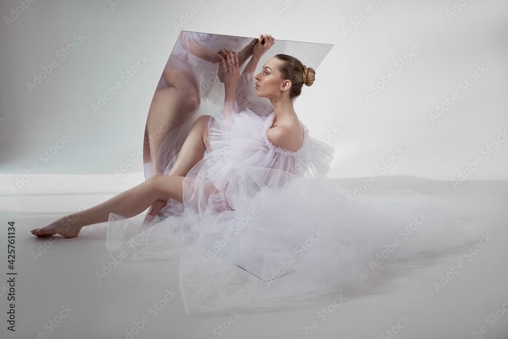 Naklejka premium Romantic beauty woman in a light transparent dress is reflected in a flexible mirror sitting on the floor. Perfect body and long legs