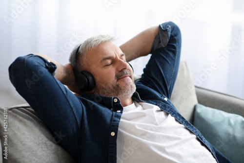 Joyful senior man reclining on couch, listening to music