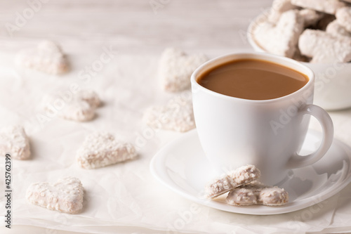 Photo of a vegan breakfast. White cup of coffee with almond milk. Vegan coconut cookies are nearby. Heart-shaped white cookies. On a white background close up.