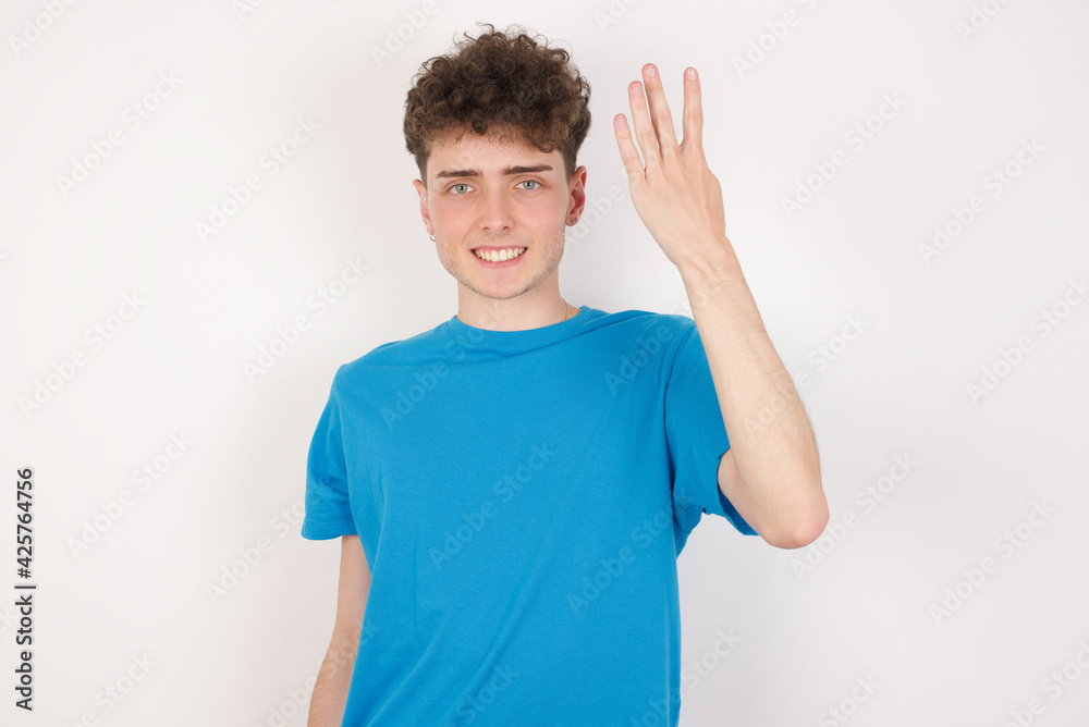 young caucasian handsome man with curly hair wearing blue T-shirt against white studio background smiling and looking friendly, showing number four or fourth with hand forward, counting down