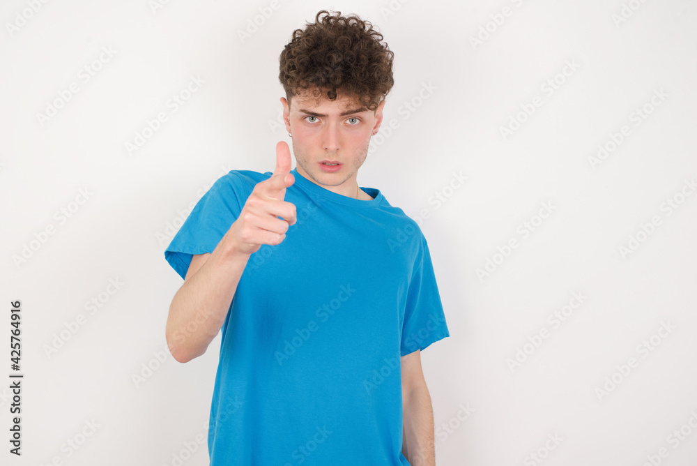 Shocked young caucasian handsome man with curly hair wearing blue T-shirt against white studio background points at you with stunned expression Shocked young caucasian handsome man with curly hair wearing blue T-shirt against white studio background points at you with stunned expression