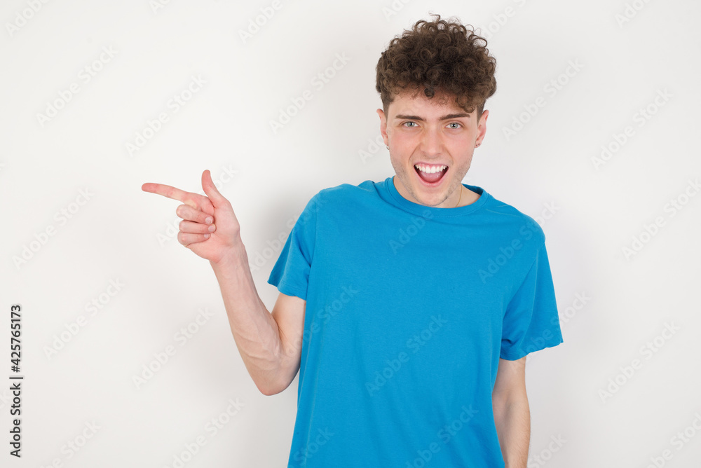 young caucasian handsome man with curly hair wearing blue T-shirt against white studio background points aside on copy blank space. People promotion and advertising concept young caucasian handsome man with curly hair wearing blue T-shirt against white studio background points aside on copy blank space. People promotion and advertising concept