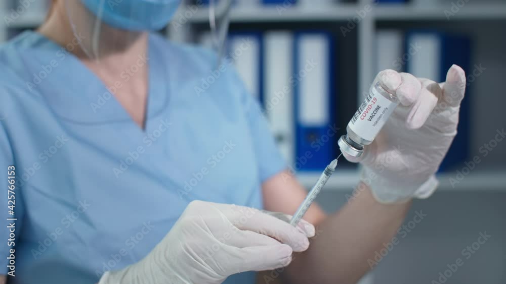 treatment coronavirus, masked physician in blue uniform and protective gloves with syringe pierces the rubber seal of the glass ampoule and receives the medicine treatment coronavirus, masked physician in blue uniform and protective gloves with syringe pierces the rubber seal of the glass ampoule and receives the medicine