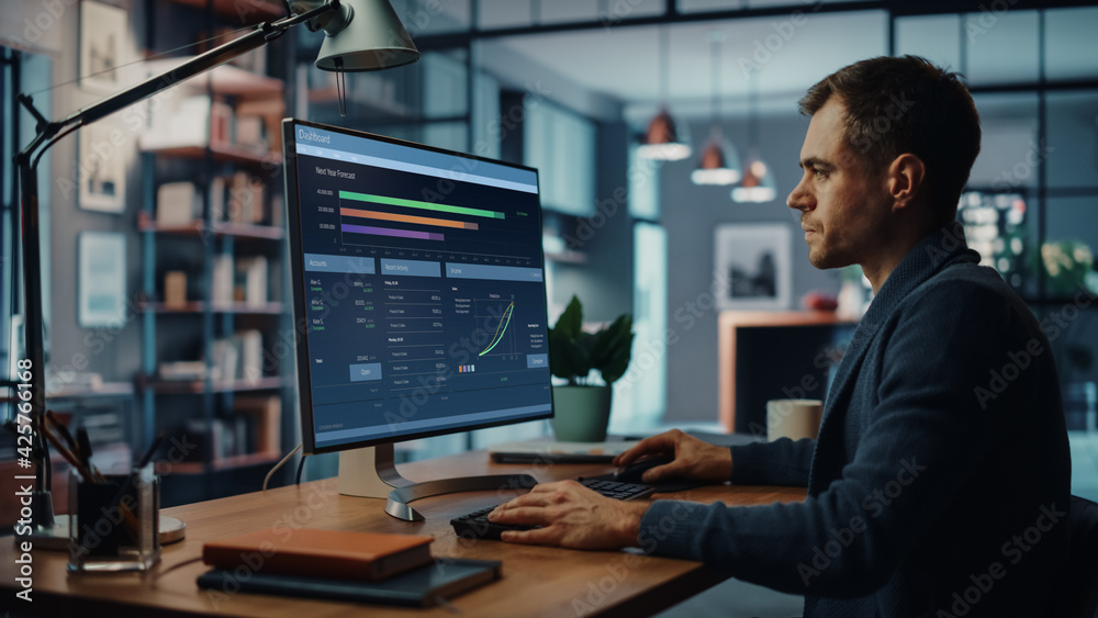 Handsome Caucasian Male Specialist Working on Desktop Computer in Creative Home Living Room. Freelance Male is Doing Market Analysis and Creates Report with Charts for Clients and Employer.