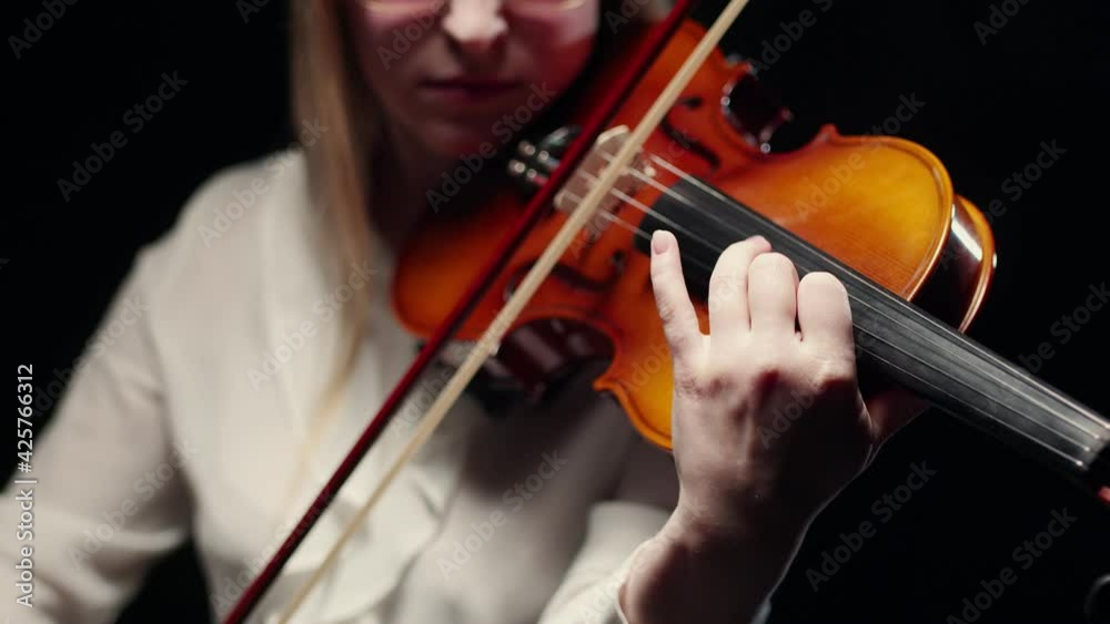Woman violinist plays the violin with a bow and fingers on the strings in studio, a dark background. Symphony orchestra. Woman violinist plays the violin with a bow and fingers on the strings in studio, a dark background. Symphony orchestra.