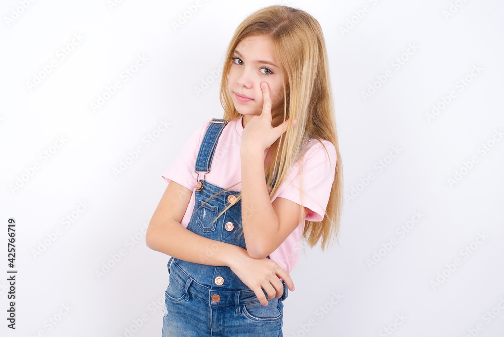 beautiful caucasian little girl wearing denim jeans overall over white background Pointing to the eye watching you gesture, suspicious expression. beautiful caucasian little girl wearing denim jeans overall over white background Pointing to the eye watching you gesture, suspicious expression.