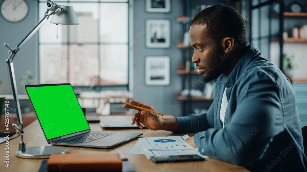 African American Man Having an Online Video Lesson on Laptop Computer with Mock Up Green Screen in Living Room. Freelancer Working on His Skills or Student Doing Homework Over the Internet.
