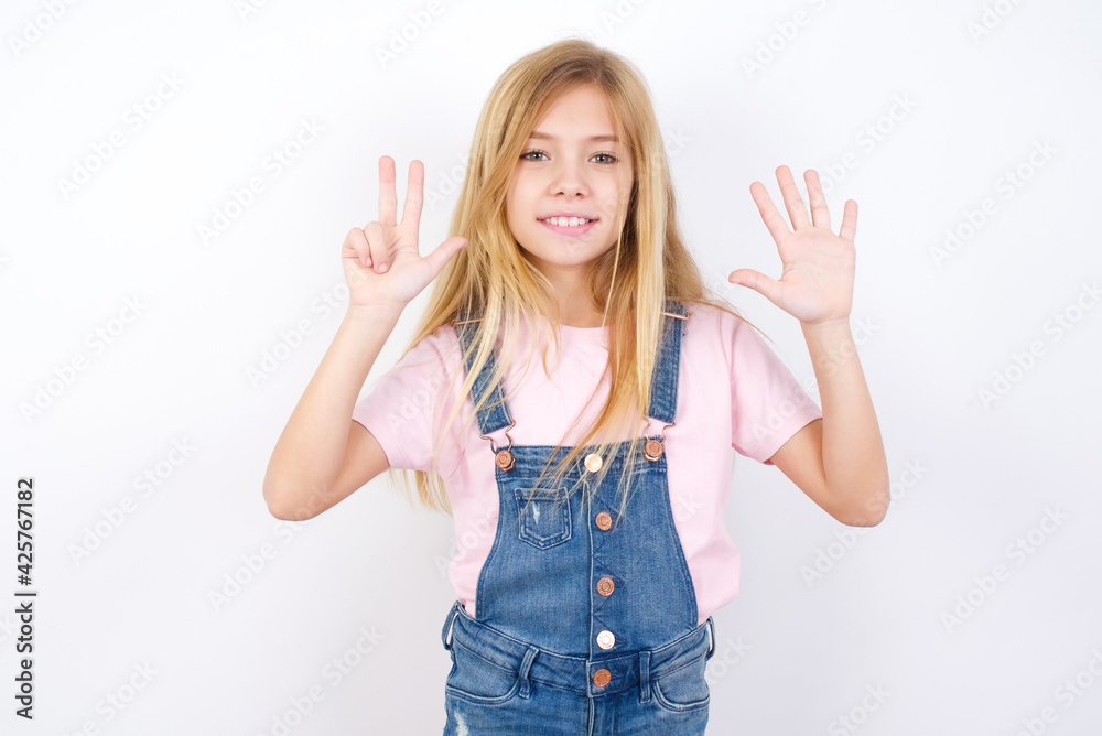 beautiful caucasian little girl wearing denim jeans overall over white background showing and pointing up with fingers number eight while smiling confident and happy. beautiful caucasian little girl wearing denim jeans overall over white background showing and pointing up with fingers number eight while smiling confident and happy.