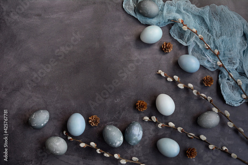 Flat lay, copy space. Easter composition on a gray background. Blue, marble and gray eggs, willow branches and a napkin. View from above