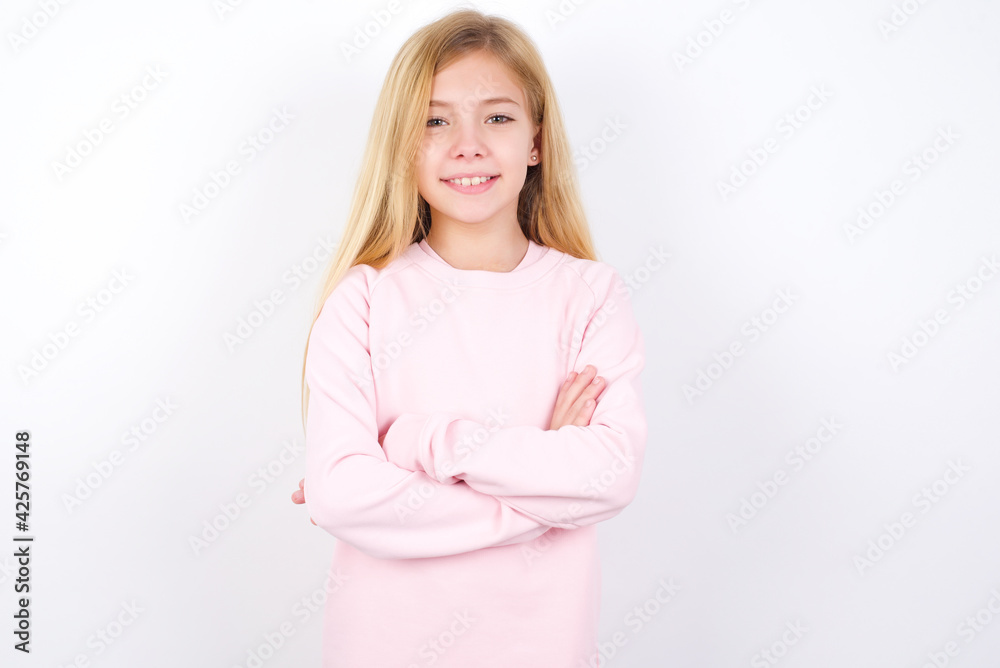 Self confident serious calm Beautiful caucasian blonde little girl wearing pink sweater stands with arms folded. Shows professional vibe stands in assertive pose. Self confident serious calm Beautiful caucasian blonde little girl wearing pink sweater stands with arms folded. Shows professional vibe stands in assertive pose.