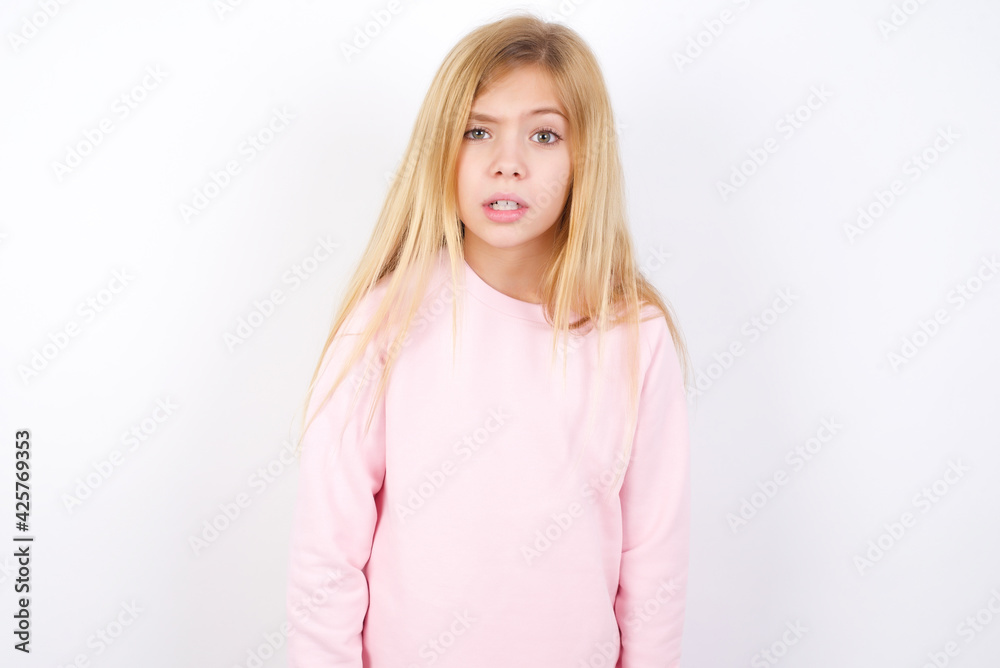Portrait of dissatisfied Beautiful caucasian blonde little girl wearing pink sweater smirks face, purses lips and looks with annoyance at camera, discontent hearing something unpleasant Portrait of dissatisfied Beautiful caucasian blonde little girl wearing pink sweater smirks face, purses lips and looks with annoyance at camera, discontent hearing something unpleasant