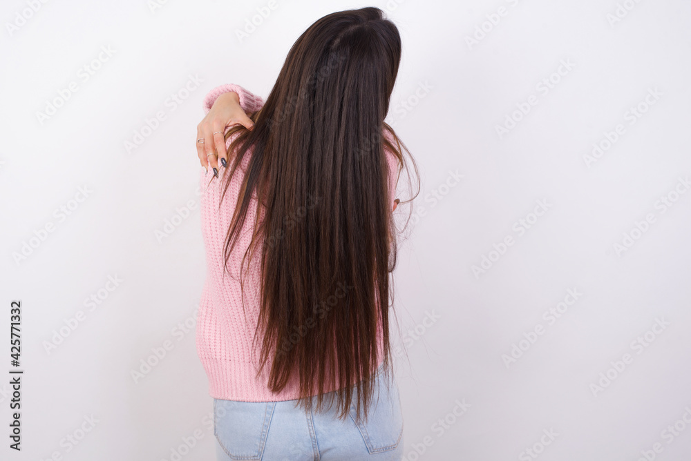 young beautiful caucasian woman wearing pink knitted jacket over white wall hugging herself happy and positive from backwards. Self love and self care young beautiful caucasian woman wearing pink knitted jacket over white wall hugging herself happy and positive from backwards. Self love and self care