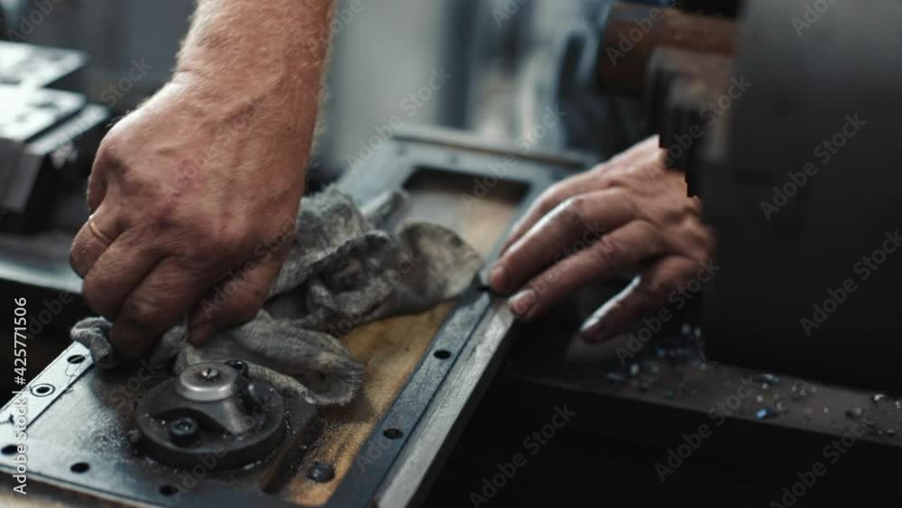 Service and repair of machine tools in a machine shop or workshop. These are the hands of a white man with a rag wiping the metal parts of a lathe engine with grease. The work of a locksmith on Service and repair of machine tools in a machine shop or workshop. These are the hands of a white man with a rag wiping the metal parts of a lathe engine with grease. The work of a locksmith on