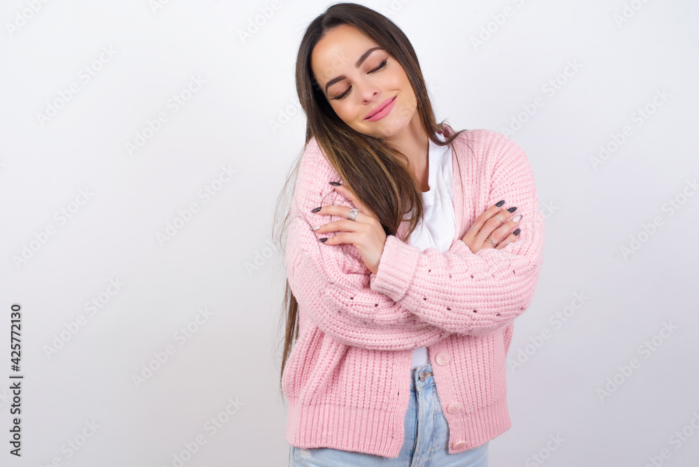 young beautiful caucasian woman wearing pink knitted jacket over white wall Hugging oneself happy and positive, smiling confident. Self love and self care young beautiful caucasian woman wearing pink knitted jacket over white wall Hugging oneself happy and positive, smiling confident. Self love and self care