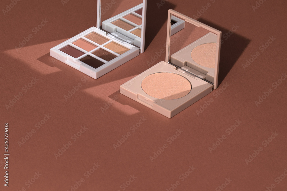 Eye shadow palette and highlighting powder on pink clean background with hard light. Sunlight