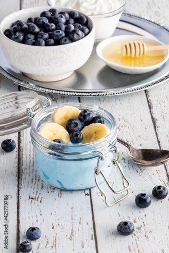A blue spirulina yogurt parfait with a tray of the ingredients to make the parfait, in behind.