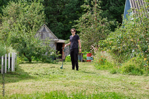 a young man cuts the grass with a trimer at his summer cottage © Елена Гурова