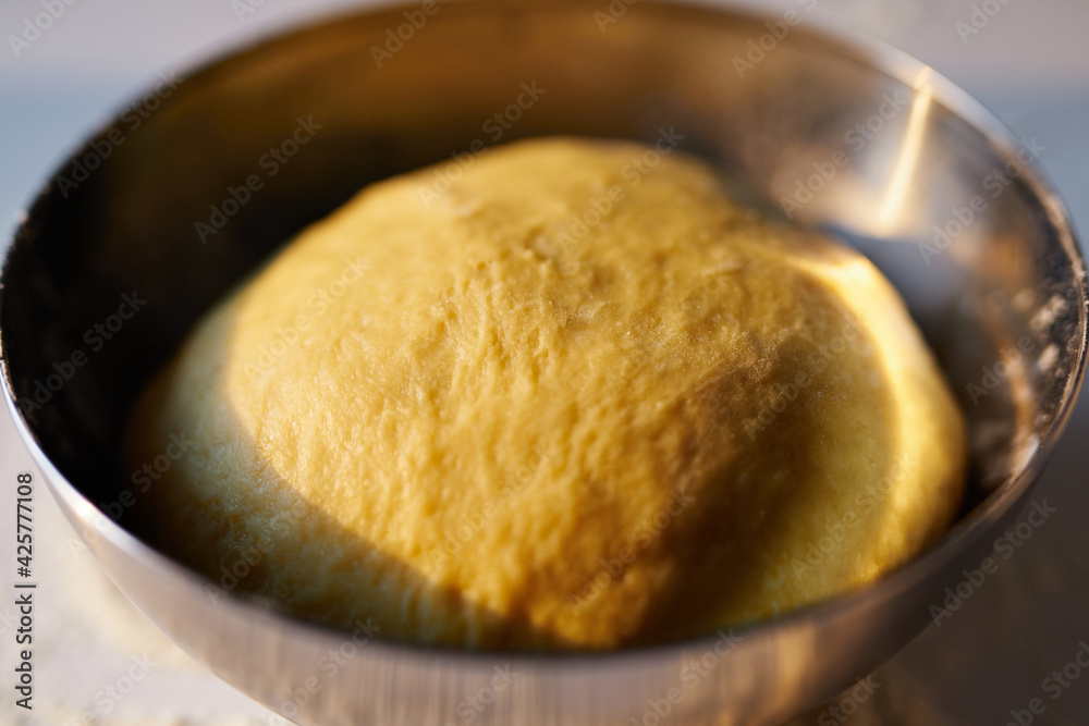 Baking, pie or Easter pastry making concept. Freshly made bread dough proofing in the kitchen in stainless steel bowl in sunset sunlight. High quality photo