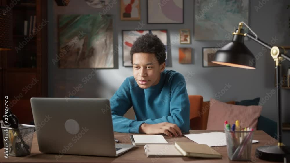Black teenager man on video conference call waving his hand, camera view, video chat, african american male chatting with friends, smiling, communication during coronavirus lockdown, remote learning. Black teenager man on video conference call waving his hand, camera view, video chat, african american male chatting with friends, smiling, communication during coronavirus lockdown, remote learning.