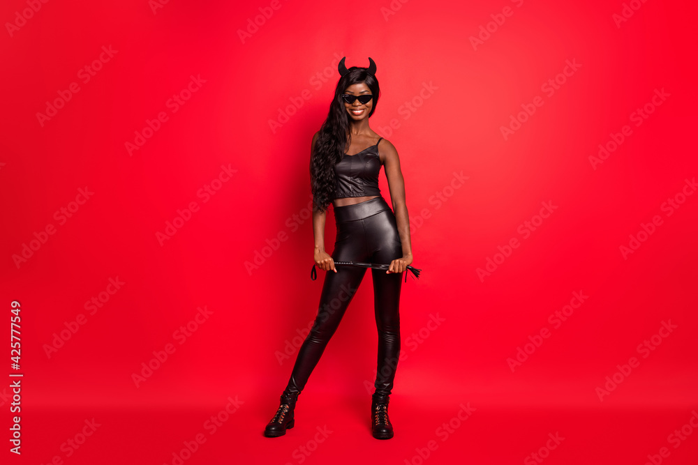 Full length photo portrait of african american horned girl with leather whip isolated on bright red colored background