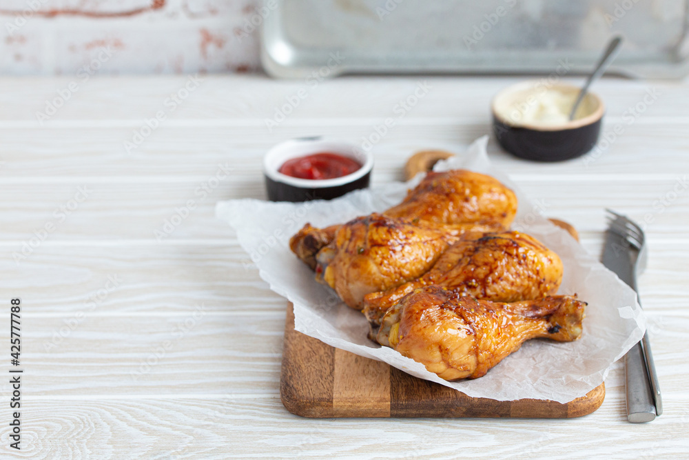 Roasted golden chicken legs drumsticks on baking paper on wooden board served with ketchup and mayonnaise on rustic white wooden table, angle view with space for text Roasted golden chicken legs drumsticks on baking paper on wooden board served with ketchup and mayonnaise on rustic white wooden table, angle view with space for text