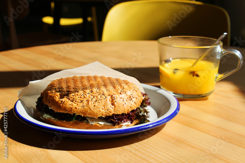 Tasty burger with lettuce. Delicious grilled bun with seasam seeds and yellow fruit tea on a wooden table  photo