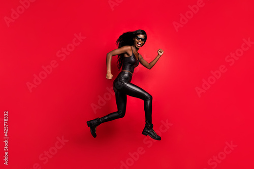 Full length body size profile side view of funky girl wear leather suit jumping running action isolated on bright red color background
