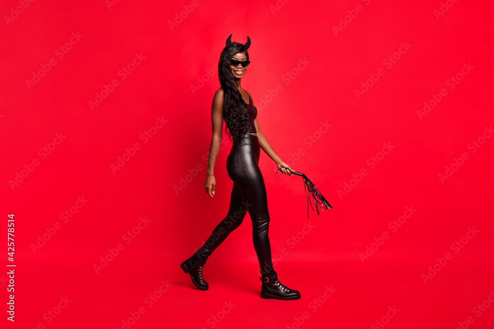 Full length body size profile side view of gorgeous kinky cheerful girl going holding whip isolated over bright red color background Full length body size profile side view of gorgeous kinky cheerful girl going holding whip isolated over bright red color background